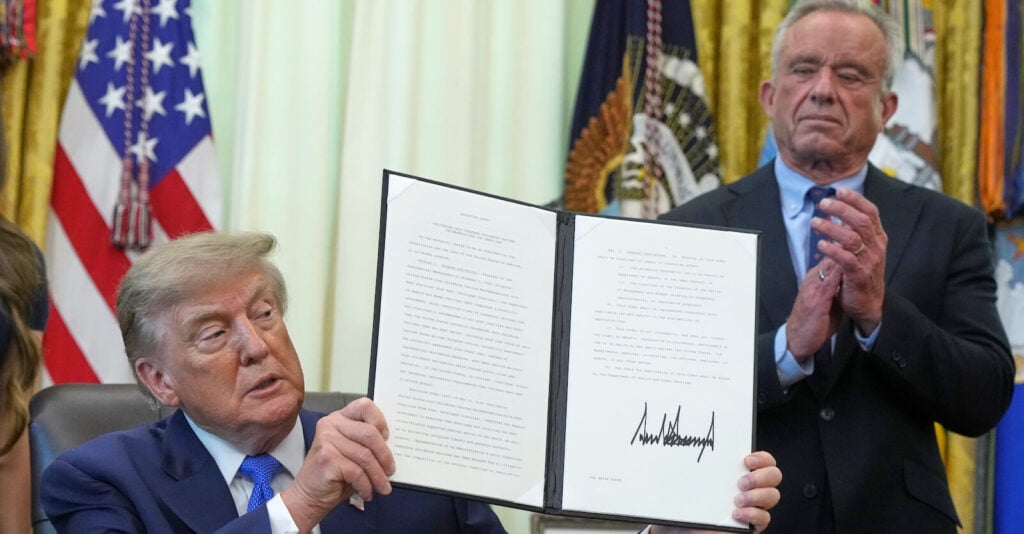 President Trump, seated, holds up the signed August 10, 2026 executive order while Robert F. Kennedy Jr. applauds in the background