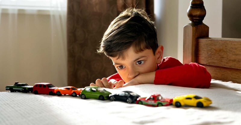 boy lining up a row of toy cars