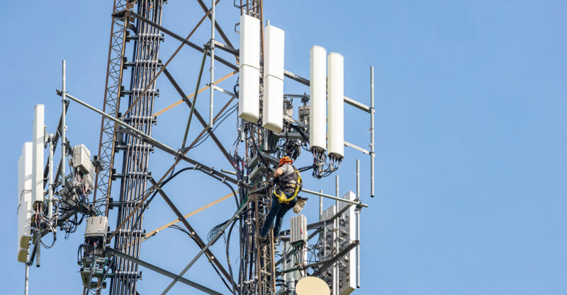 Man climber on cell phone tower against blue sky background