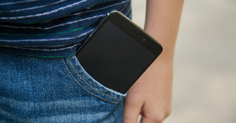 Closeup view of modern black smartphone with blank touch screen inside of pocket of blue denim jeans.