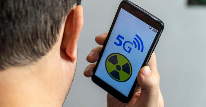 Man holding a smart phone near his head with a radiation warning symbol on the screen of the phone.