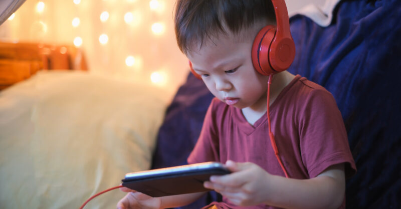 2 -3 years old toddler boy child listening to music with headphones from smartphone.