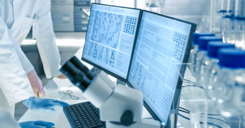 Senior Female Scientist Discusses Scientific Data with Her Laboratory Assistant. They're looking at Two Displays in a Modern Laboratory.
