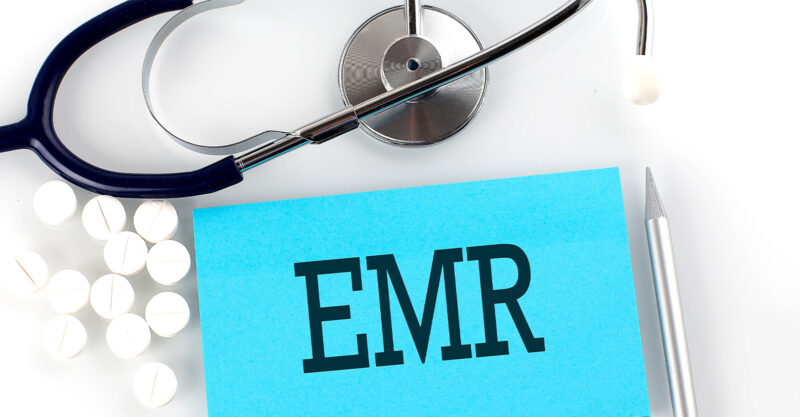 Text EMR on a table with a stethoscope, pills and pen.