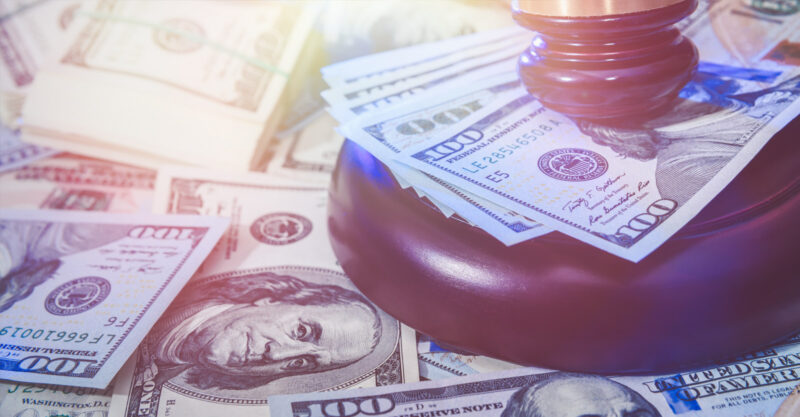 Judge hammer sitting on top of one hundred dollar bills.