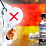 germany flag and covid vaccine with doctor holding up sign with "x" on it
