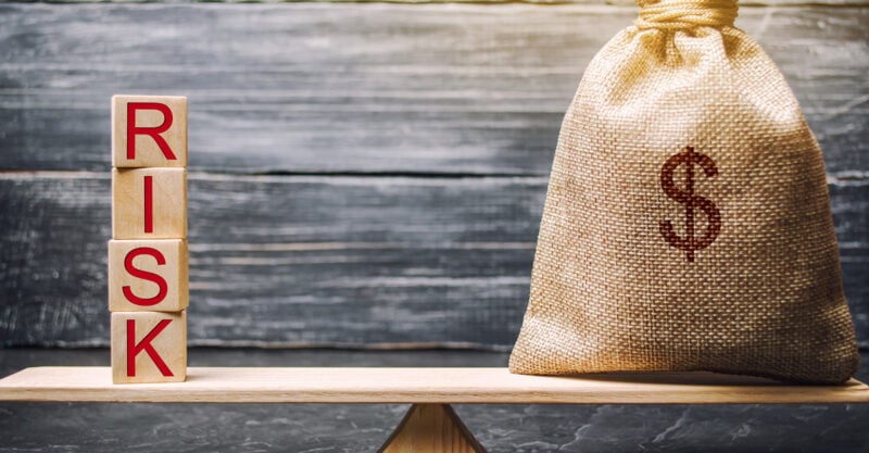 Photo of stacked blocks spelling the work Risk next to a bag with a money sign.