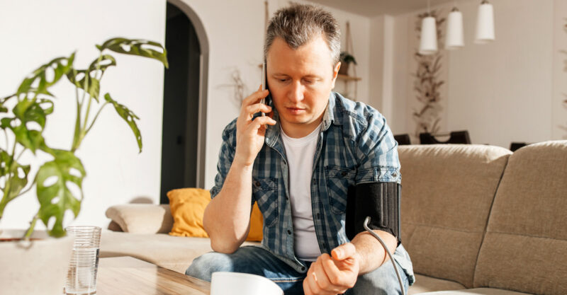Man talking on cell phone while checking blood pressure.