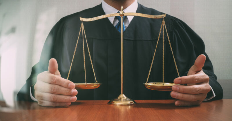 Male judge in a courtroom with the balance scale on wood table