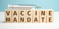 Image of Vaccine Mandate spelled out in wooden blocks with a syringe on top.
