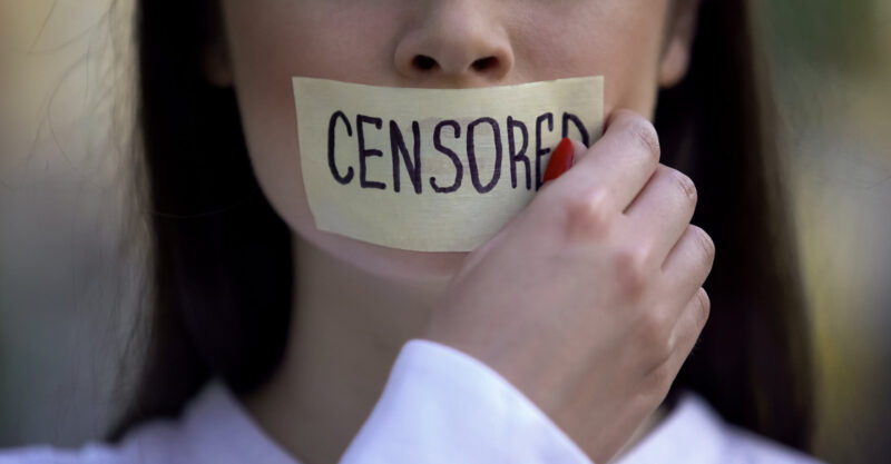 Woman taking off tape with censored word over mouth.