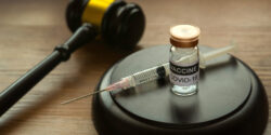 Photo of a bottle of covid-19 vaccine, gavel and syringe on wooden background.
