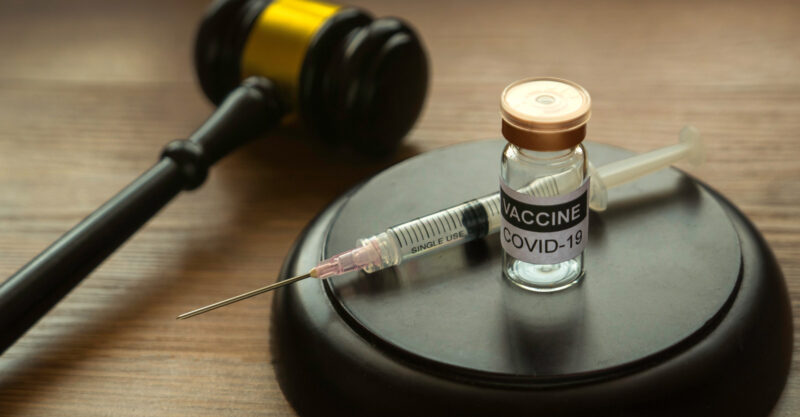 Photo of a bottle of covid-19 vaccine, gavel and syringe on wooden background.