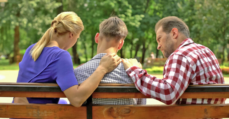 parents sitting on a bench with their son in the park