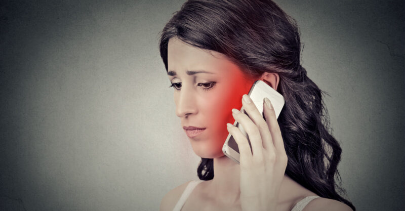 Concerned young woman talking on mobile phone having pain headache