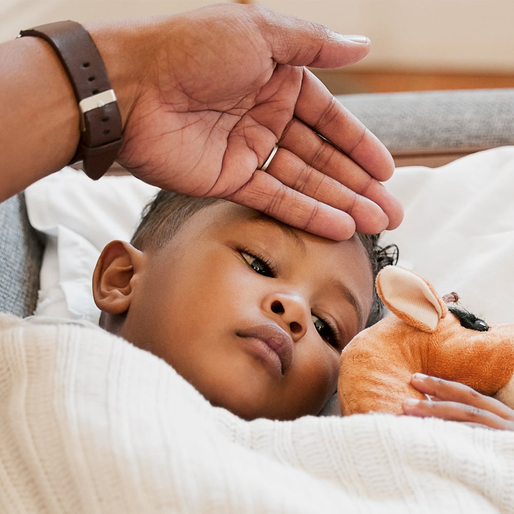 Child in bed with mother holding hand to his forehead checking for a fever.