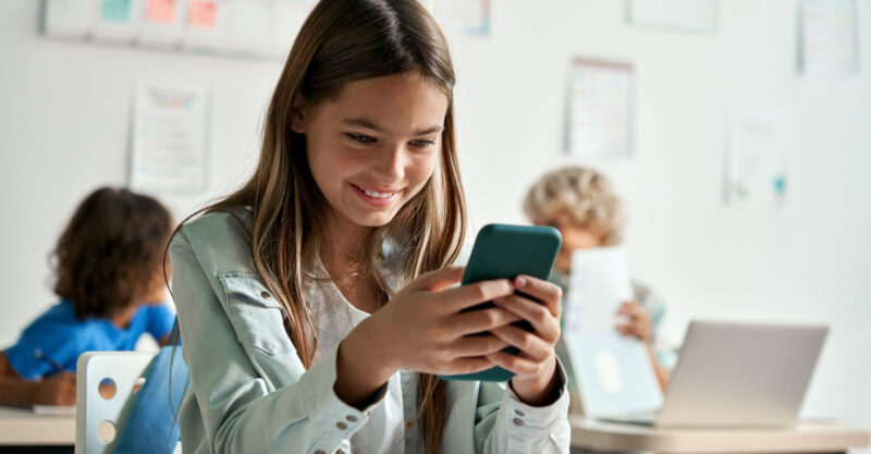 Girl on cell phone at desk in school classroom.