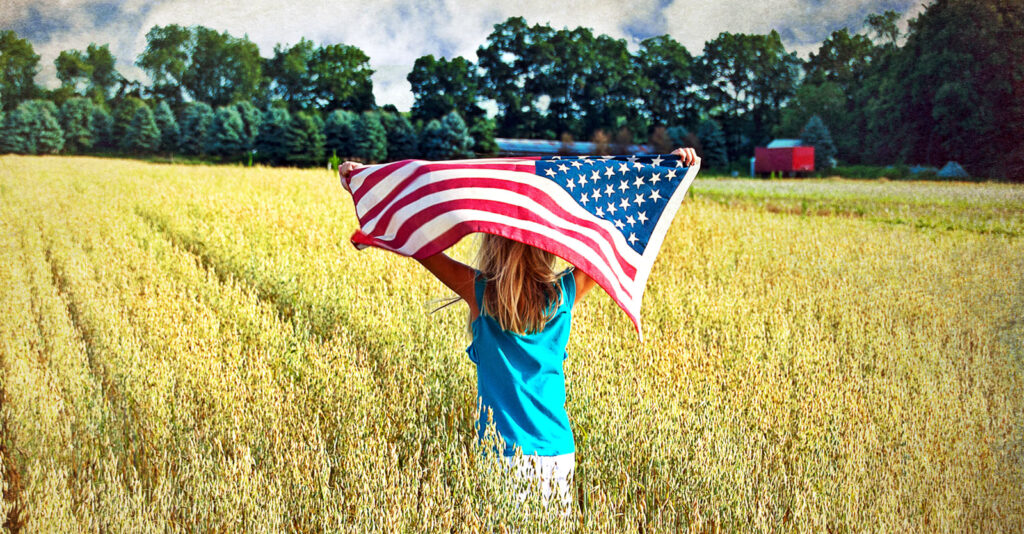 little girl holding American flag in a field outside