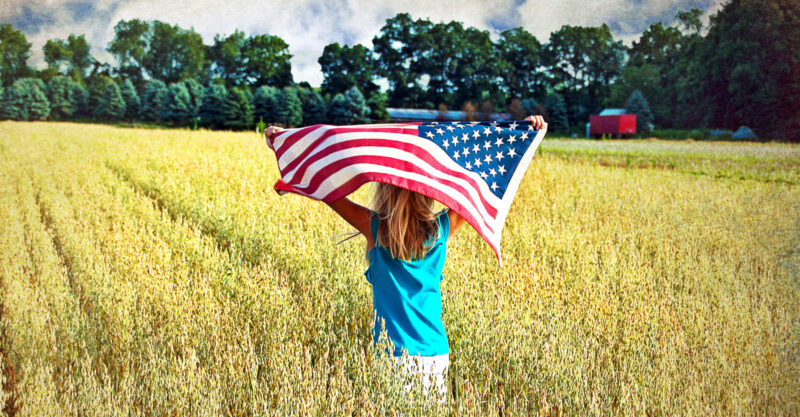 little girl holding American flag in a field outside
