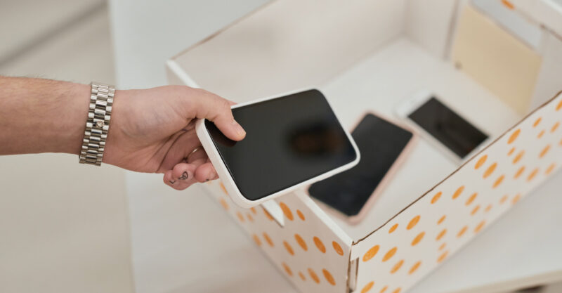 Close up of unrecognizable teenager putting smartphone in box in no gadget classroom at school.
