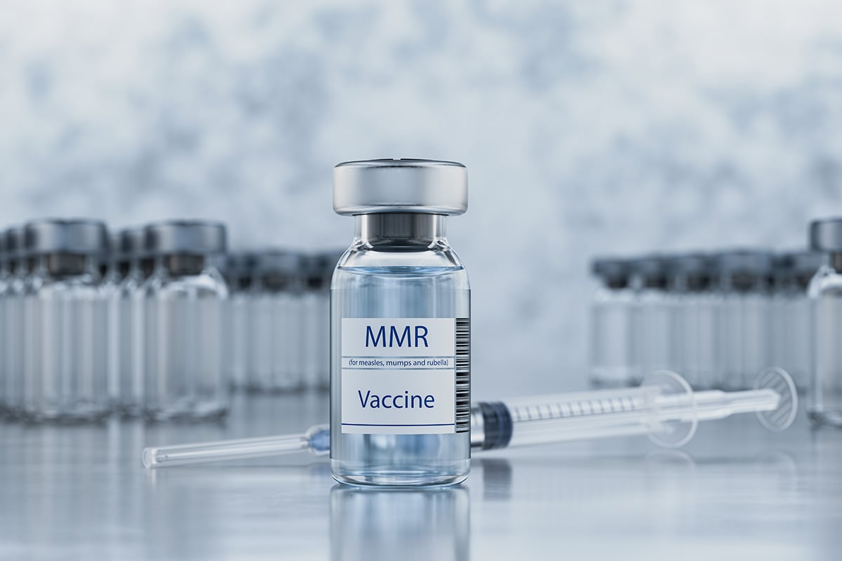 Syringe with MMR vaccine ampoules on a metal table.