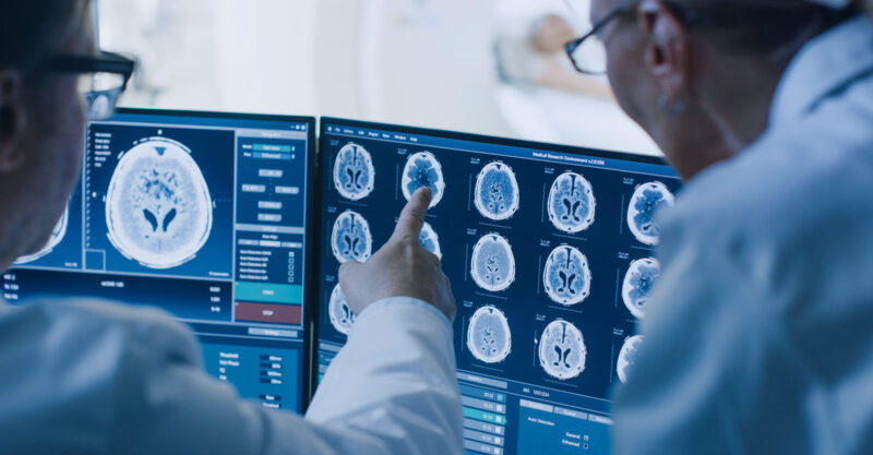 In Control Room Doctor and Radiologist Discuss Diagnosis while Watching Procedure and Monitors Showing Brain Scans Results