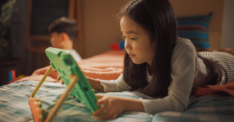 Asian Girl Using a Tablet Computer at Home in Her Bedroom